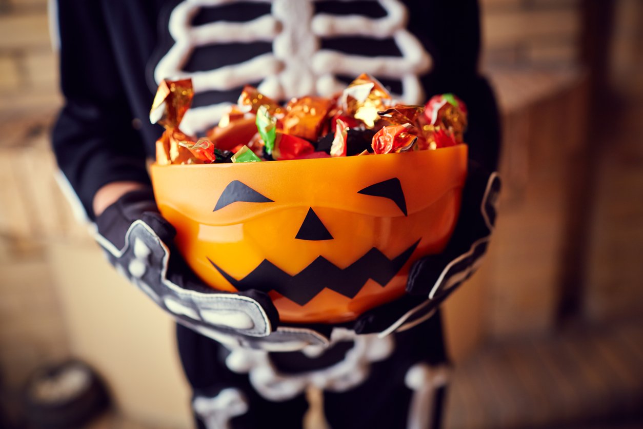 Child in skeleton costume holding full bowl of Halloween candy