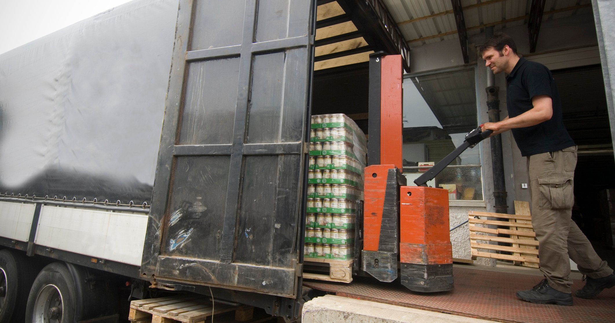 Man using a pallet mover to move canned goods on a truck