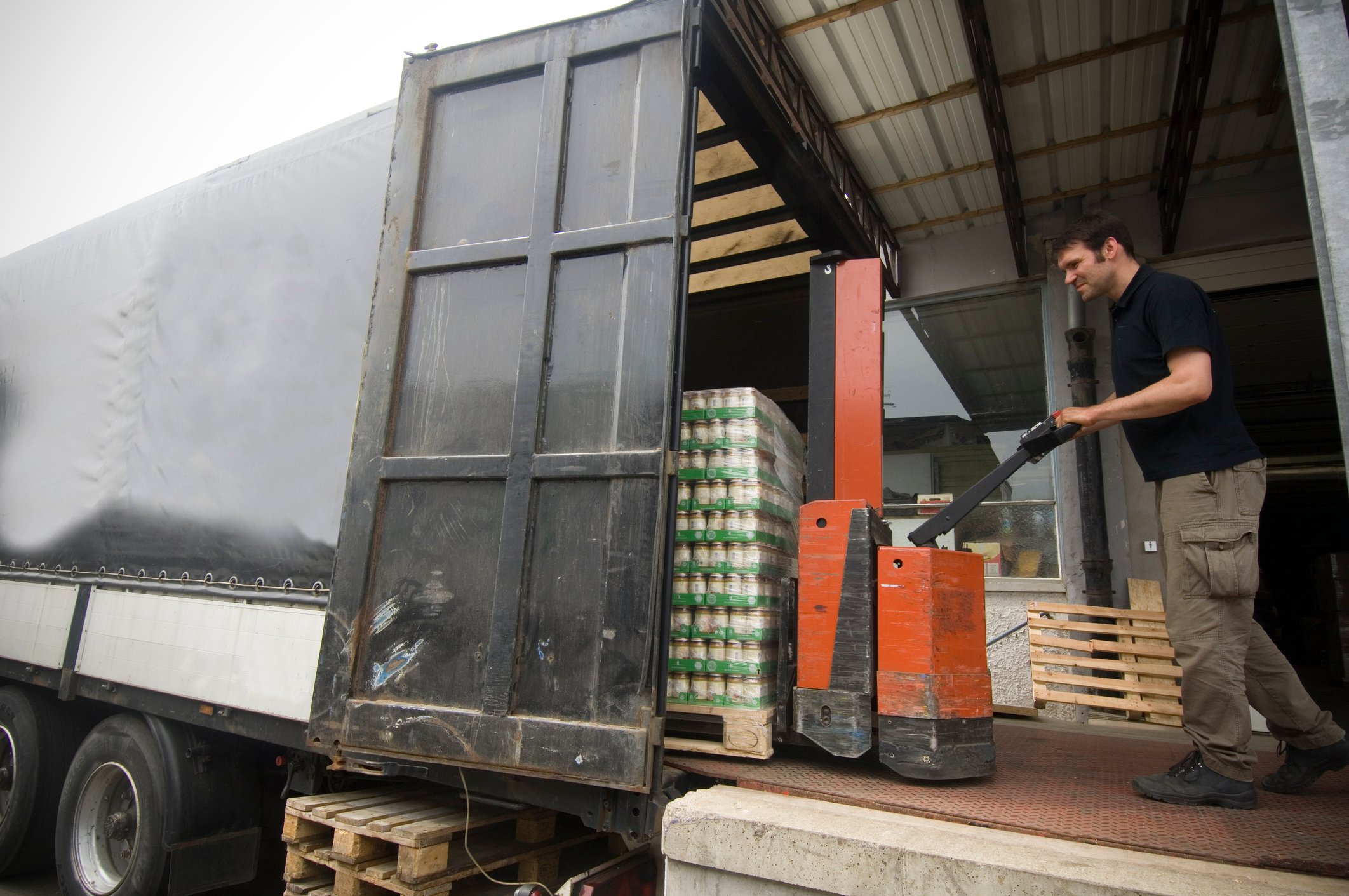 man moving pallets of canned food with a pallet mover on a truck