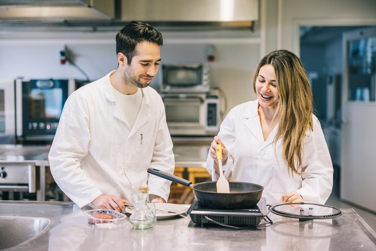 two scientists testing a recipe in a skillet in a test kitchen